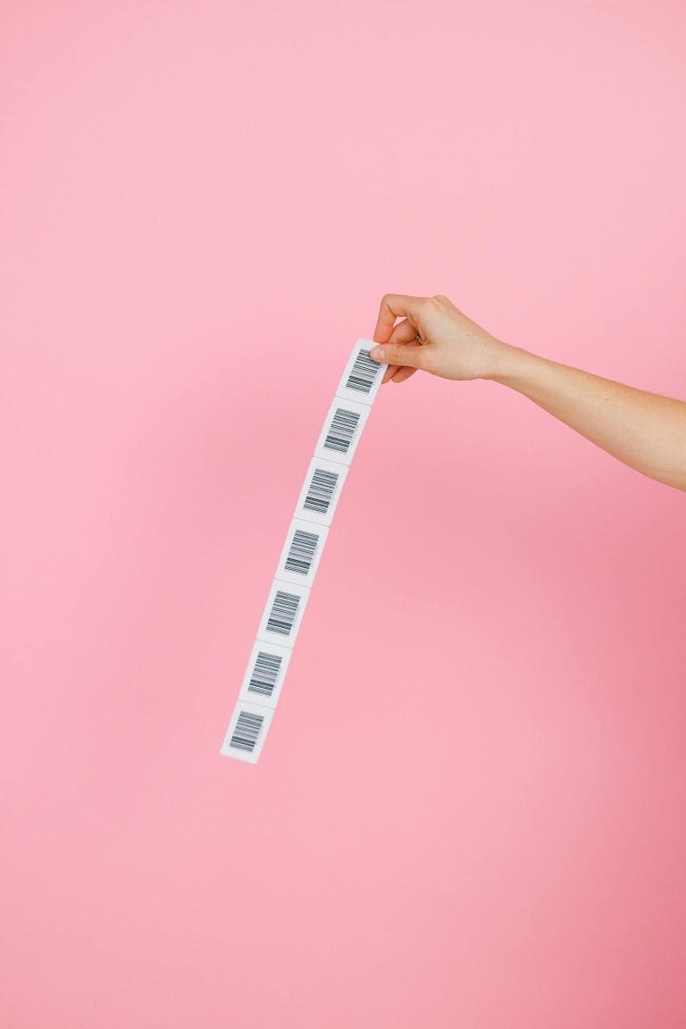 A hand holds a strip of barcodes against a pink background, creating a simple yet striking image.